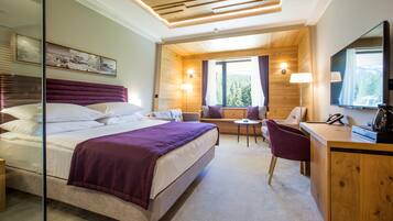 Een slaapkamer met een bed, een bureau, een stoel, een klein tafeltje en een raam met gordijnen.