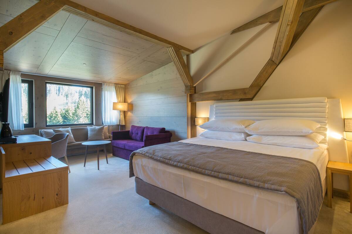 A bedroom with a large bed, a desk, a purple armchair, and a small table.
