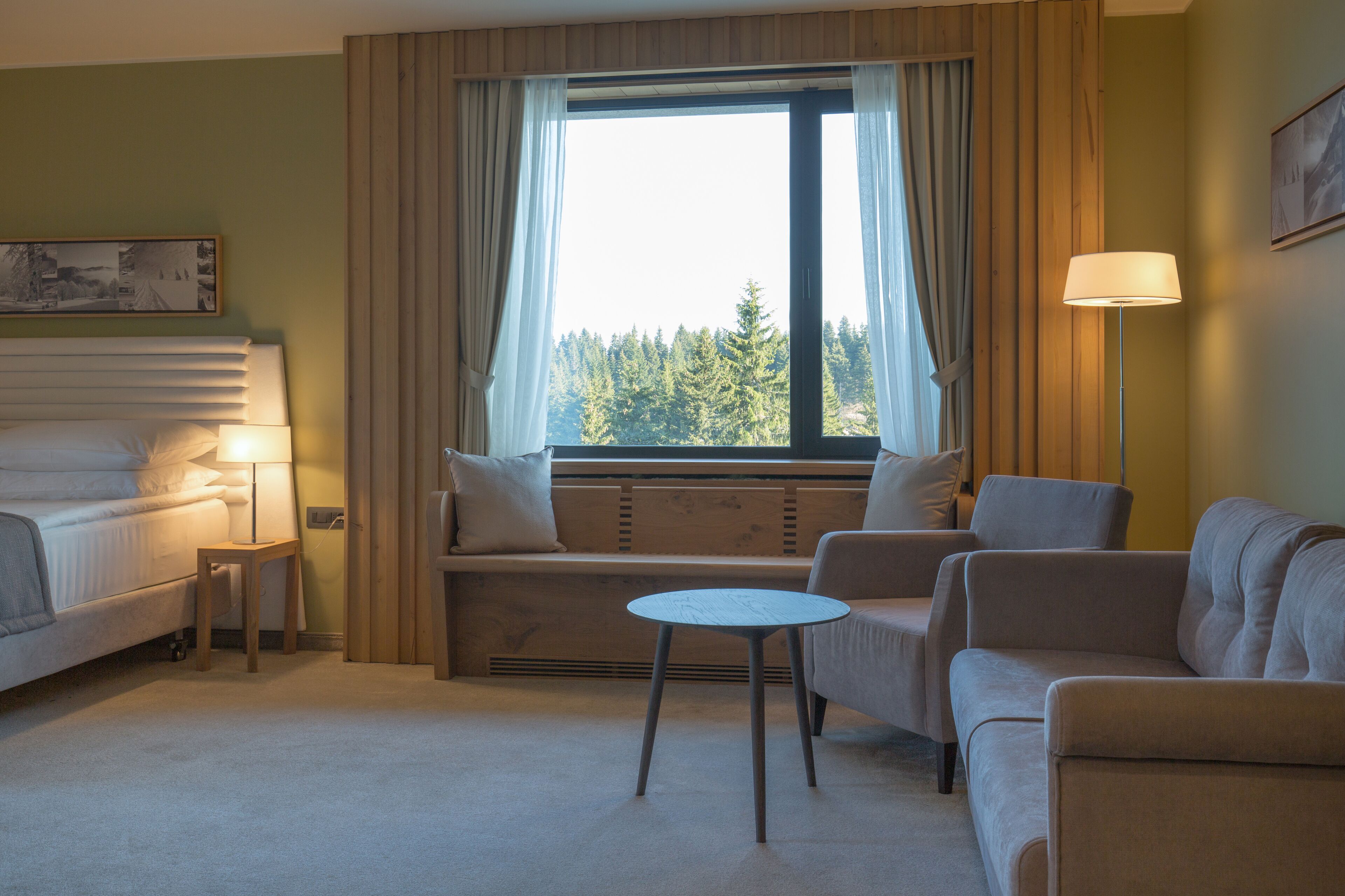 A hotel room with a bed, a sofa, a small table, a bench, and a window with curtains.