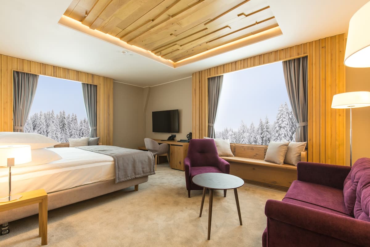 A hotel room with a bed, a desk, a chair, a sofa, and a TV.
