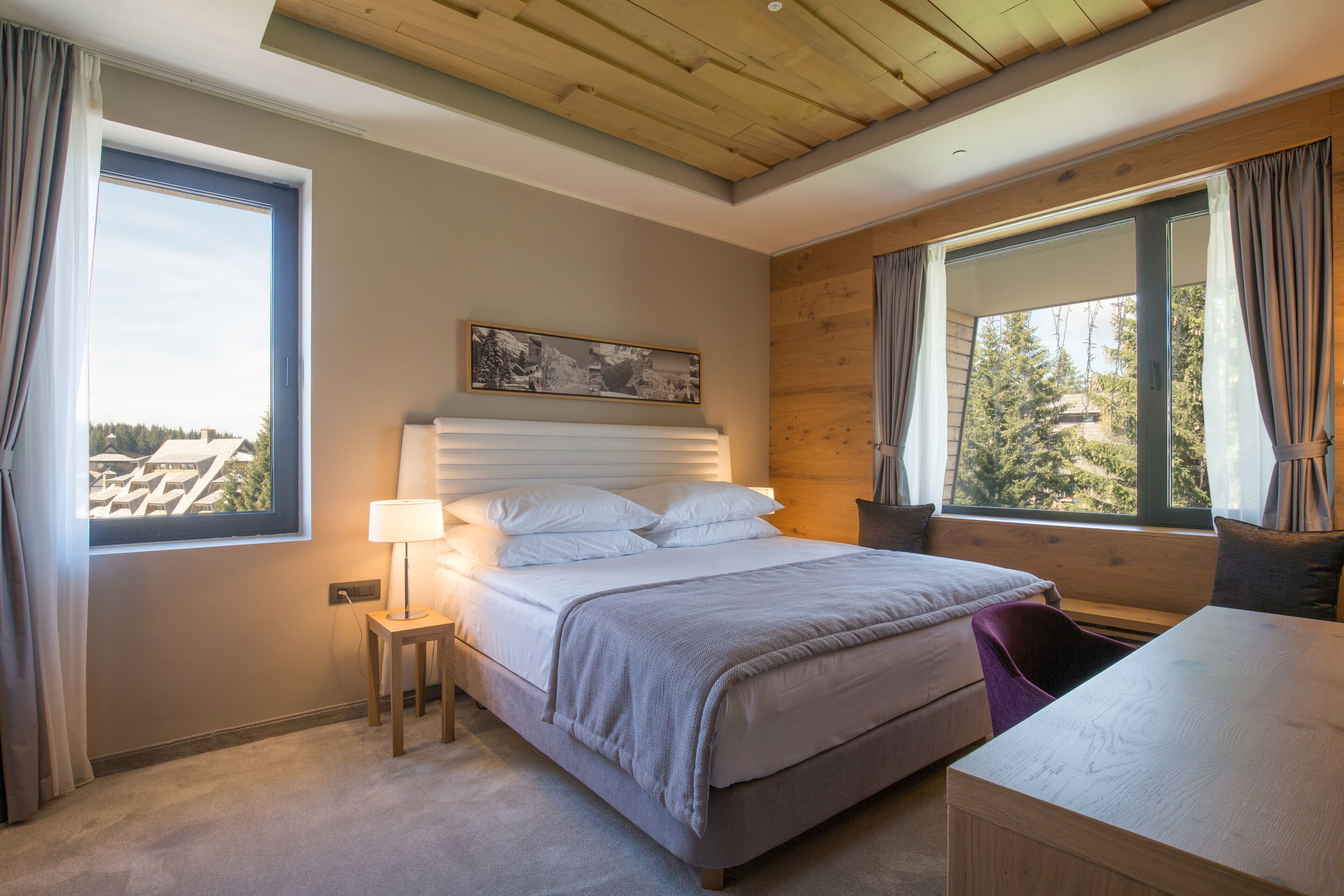 A bedroom with a large bed, a bedside table, a desk, and a window with curtains.