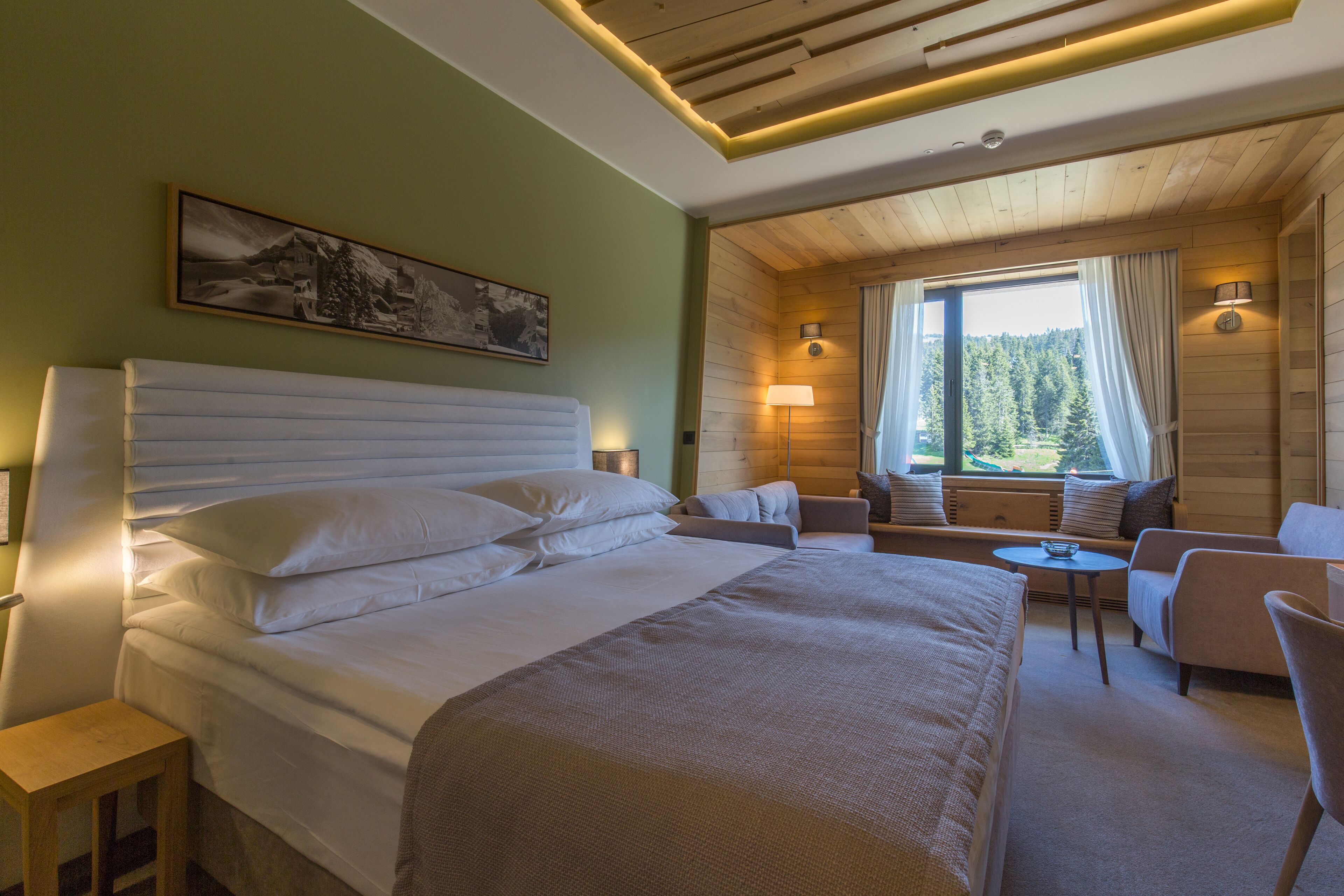 A hotel room with a large bed, a seating area with a table, and a window with a view of trees.