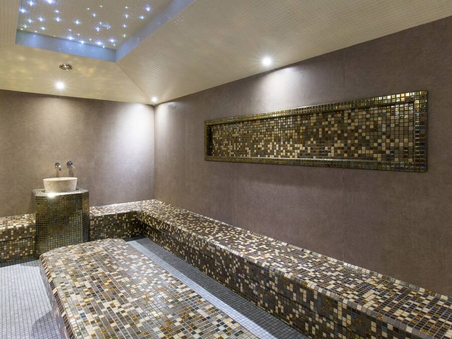 A modern spa room with a mosaic-tiled bench, a sink, and a ceiling light fixture.