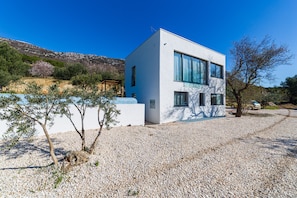 A modern two-story house with a white exterior, large windows, and a gravel driveway.
