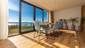 Ein moderner Essbereich mit großem Tisch und Stühlen, großen Fenstern mit Meerblick und Holzboden.