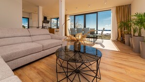Ein modernes Wohnzimmer mit einer Couch, einem Glastisch und Blick ins Freie.