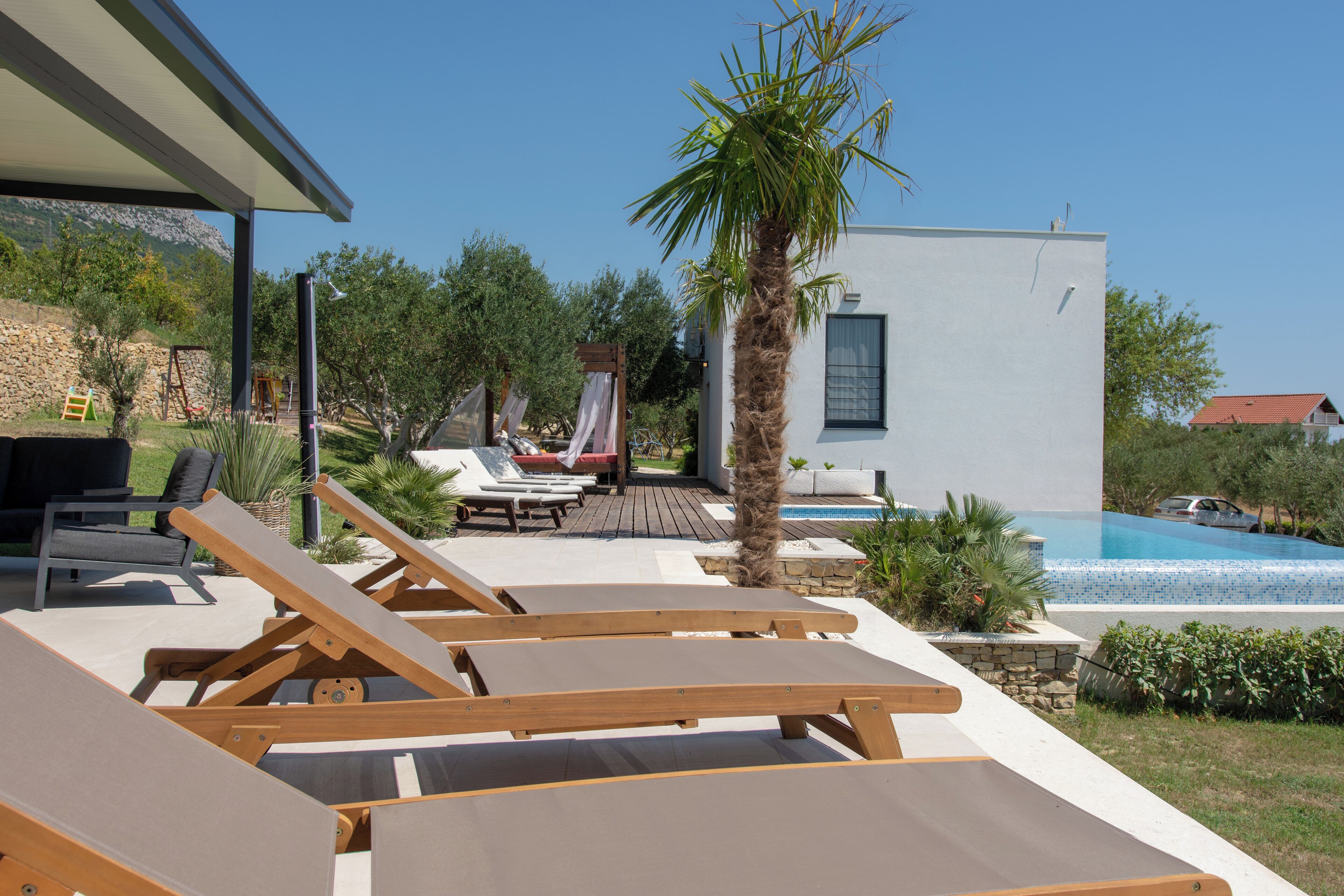 A poolside area with lounge chairs, a palm tree, and a modern building with a pool.