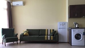 Ein kleiner Wohnraum mit Sofa, Stuhl, Waschmaschine und Kühlschrank.