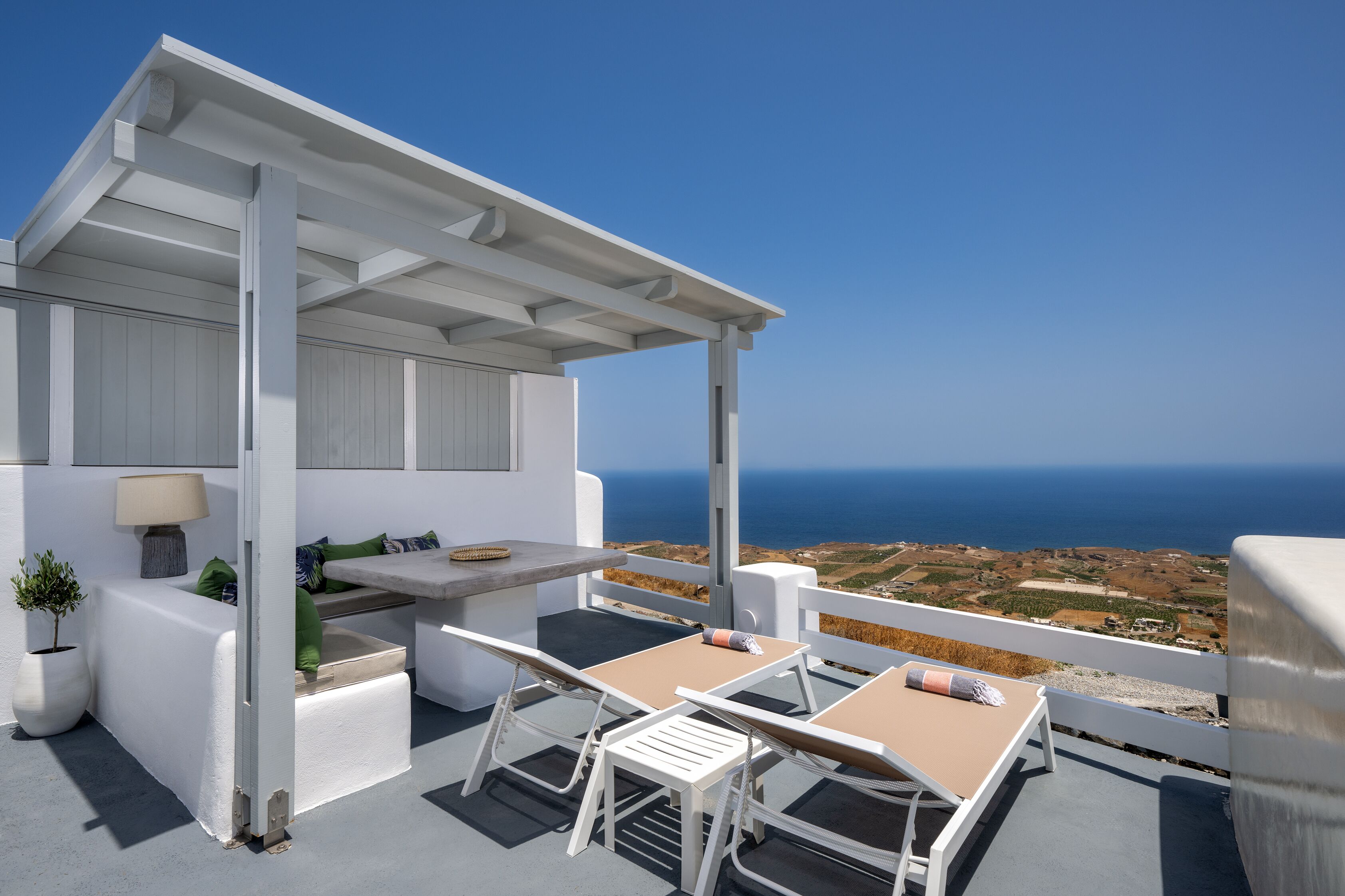 Een wit terras buiten met een tafel en stoelen, met uitzicht op een schilderachtig zeegezicht.