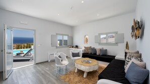 A modern living room with a view of the sea, a black sofa, white chairs, and a round coffee table.