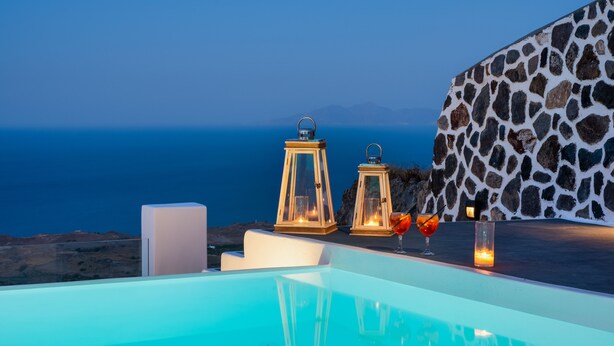 An infinity pool with a stone wall and lanterns, overlooking a coastal landscape.