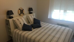 A bed with striped bedding, two pillows, a wall clock, and two bedside lamps. - Appart. 48m2 large garden terrace located 60m from the beach and 300m from the village (Mimizan Plage)