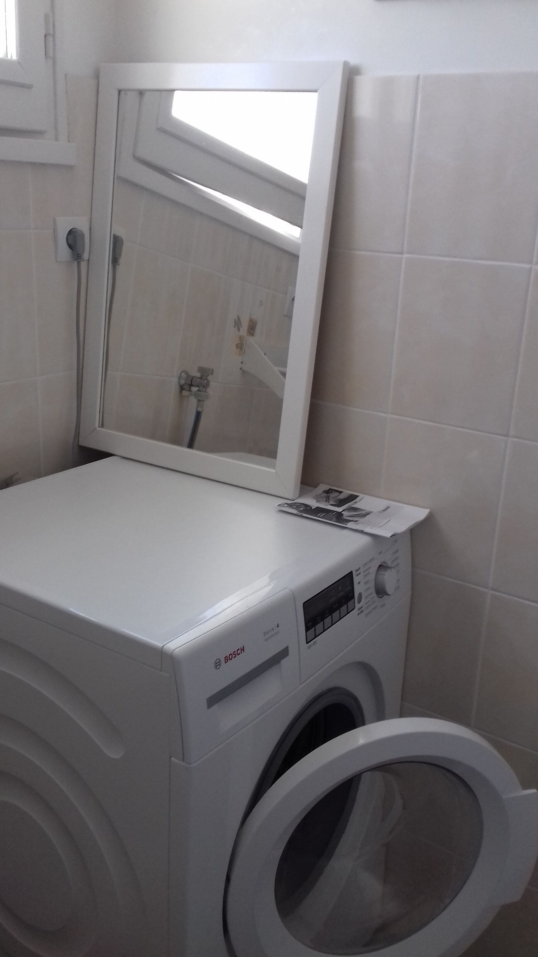 Une machine à laver Bosch blanche et compacte, à chargement frontal, dotée d’un panneau de commande et d’un miroir placé au-dessus.