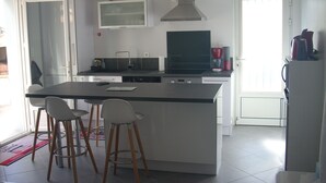 A modern kitchen with a central island, bar stools, a microwave, and a coffee maker. - Appart. 48m2 large garden terrace located 60m from the beach and 300m from the village (Mimizan Plage)
