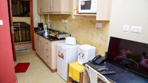 A compact kitchen with a microwave, coffee maker, and a small refrigerator. There is a TV and a laptop on the counter. - Sherry Homes West suites (Nairobi)
