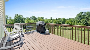 Een houten terras met een barbecue, een overdekte tafel en twee schommelstoelen.