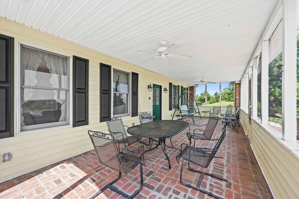 A covered patio with a brick floor, metal chairs, a round table, and a ceiling fan.