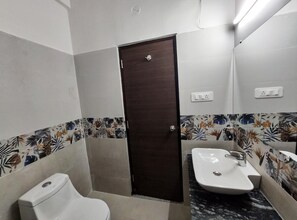 A bathroom with a toilet, sink, and a door. - Hotel The Grace (Rishikesh)