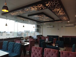 Un restaurant doté de tables hautes et de chaises rembourrées, de grandes fenêtres offrant une vue sur la ville et de motifs décoratifs au plafond.