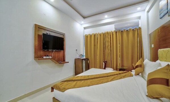 Quarto de hotel com cama, televisão na parede, mesa de cabeceira e cortina.