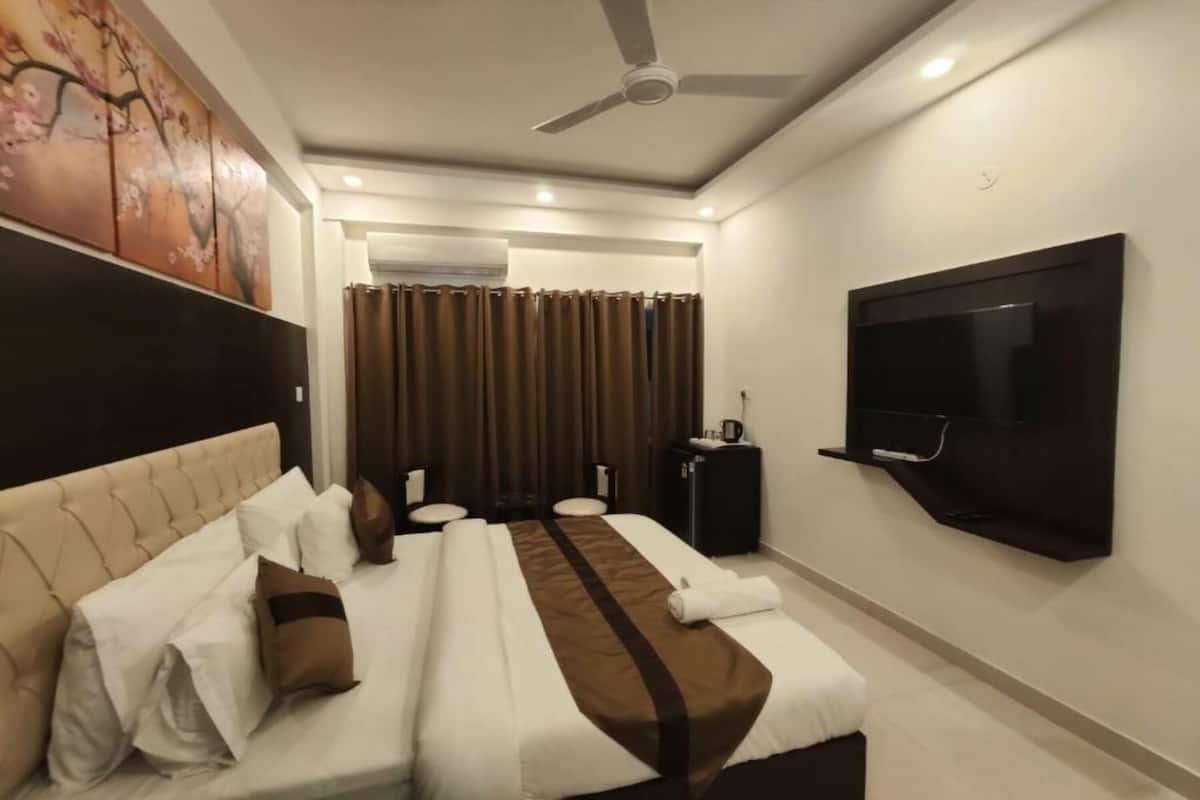 A hotel room with a large bed, a TV mounted on the wall, a ceiling fan, and a window with curtains.