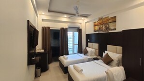 A hotel room with two beds, a ceiling fan, a TV, and a painting on the wall. - Hotel The Grace (Rishikesh)
