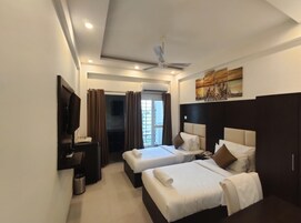 Une chambre d’hôtel avec deux lits, un ventilateur de plafond, une télévision et un tableau au mur.
