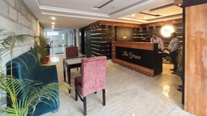 A reception area with a reception desk labeled "The Grace," a blue sofa, a pink chair, and a glass table. - Hotel The Grace (Rishikesh)