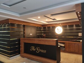 A reception area with a wooden reception desk labeled "The Grace." - Hotel The Grace (Rishikesh)