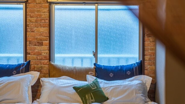 A bedroom with a brick wall, two windows, a ceiling fan, and a bed with white bedding and pillows. - A0 Kinshichou 202 (Tokyo)