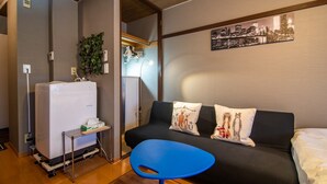 A compact hotel room with a kitchenette, a sofa with decorative pillows, a small blue table, and a cityscape artwork on the wall. - A0 Kinshichou 202 (Tokyo)