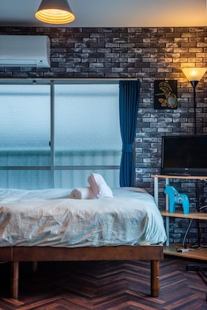 A hotel room with a bed, a TV, a lamp, and a brick wall.