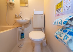 A small bathroom with a toilet, sink, and shower. There are signs on the wall and a roll of toilet paper on the wall.