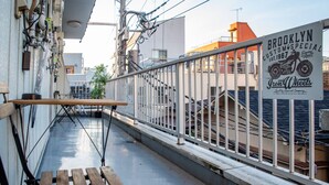 Ein schmaler Außenbereich mit einer Holzbank, einem Metallgeländer und einem Schild für Brooklyn Custom Special.