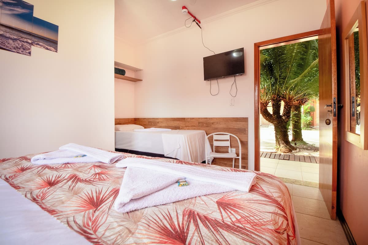 A hotel room with a bed, two bedside tables, a TV, and a view of a tree outside.