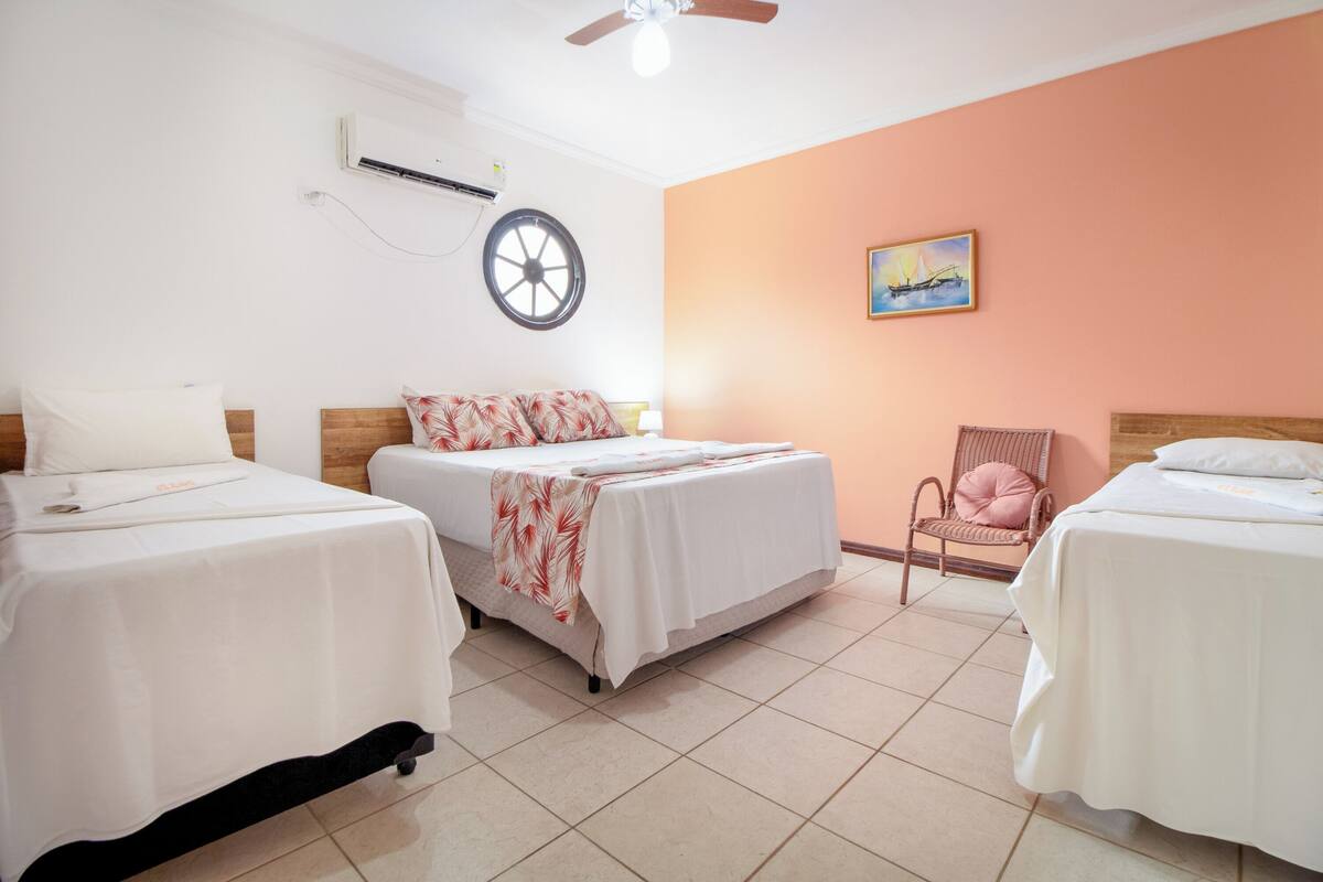A hotel room with three beds, a ceiling fan, an air conditioning unit, a wall clock, and a painting.