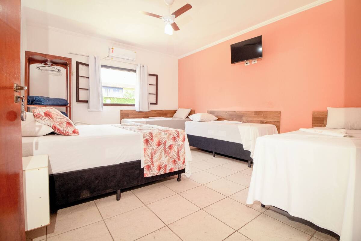 A hotel room with two beds, a television on the wall, and a window with curtains.