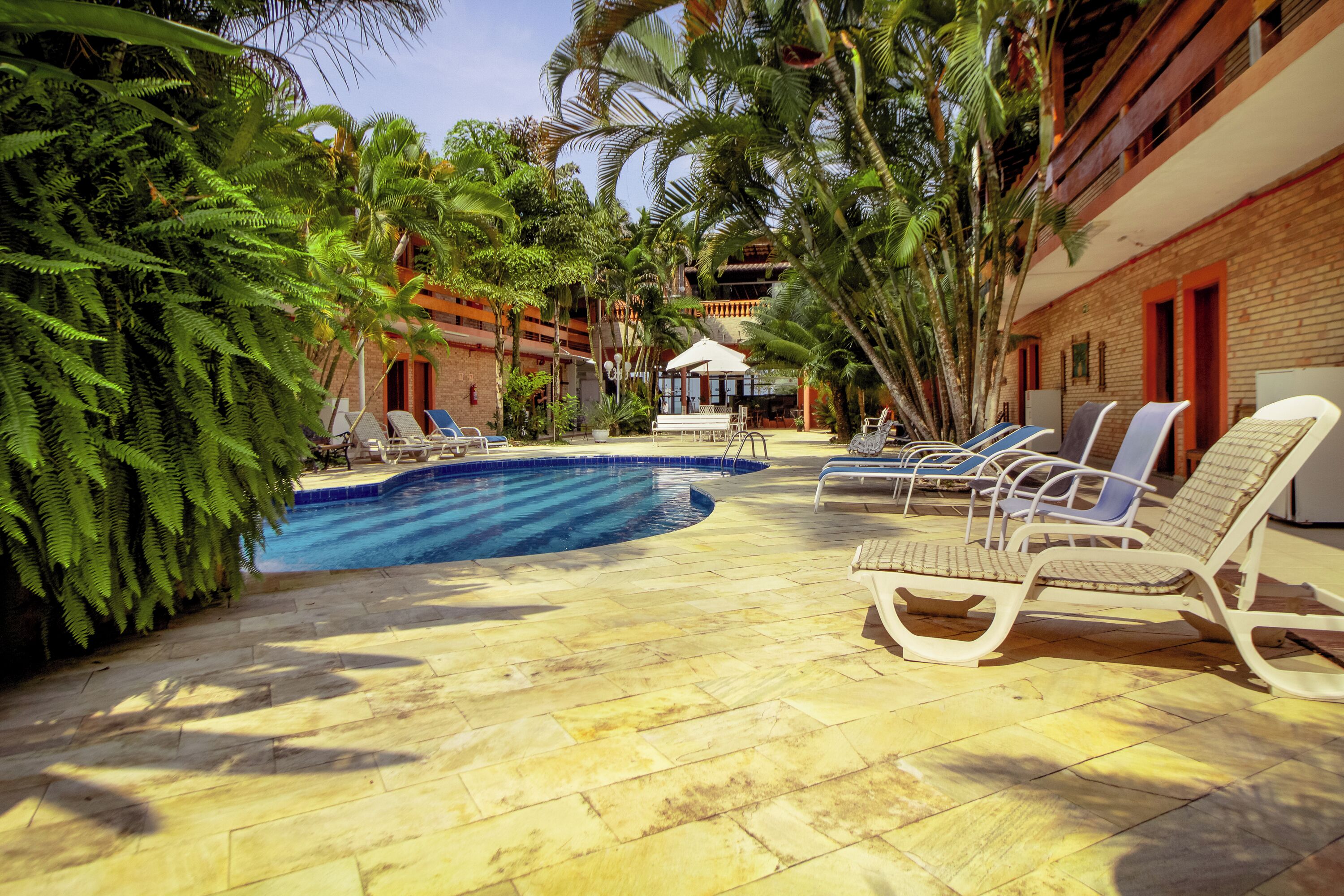 A pool area with lounge chairs, palm trees, and a building with a brick facade.
