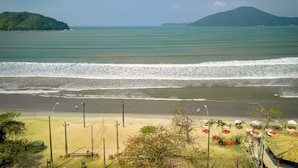 A beach with umbrellas and chairs, a sandy shore, and a view of the sea and distant hills. - Hotel Dellamares (Ubatuba)
