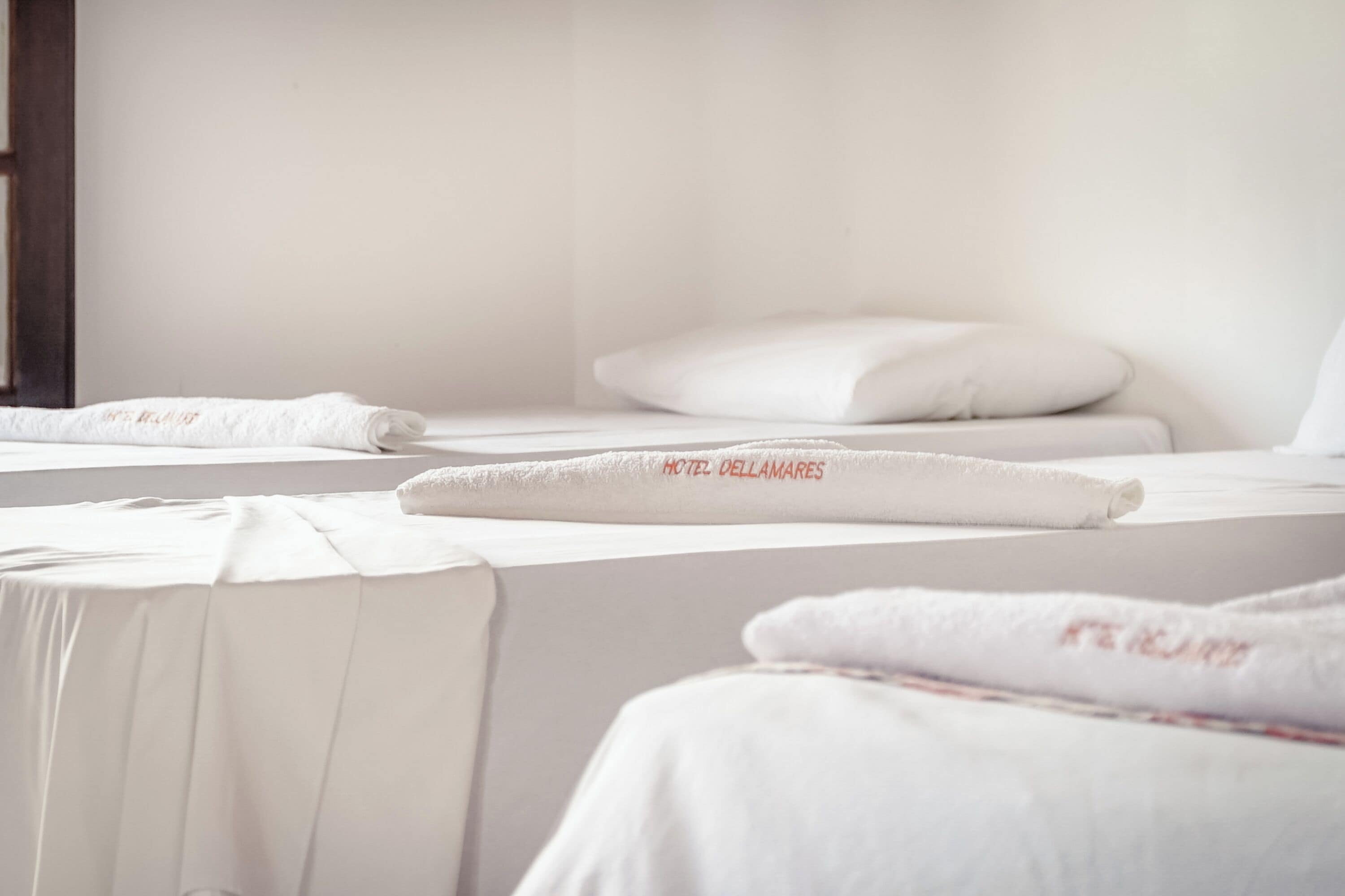 Una habitación de hotel con camas bien hechas, cada una con una colcha blanca y una toalla con el nombre del hotel.