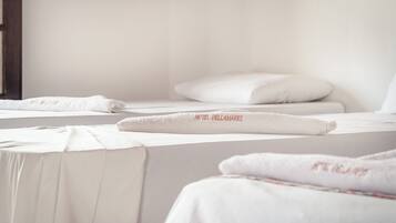 Una habitación de hotel con camas bien hechas, cada una con una colcha blanca y una toalla con el nombre del hotel.