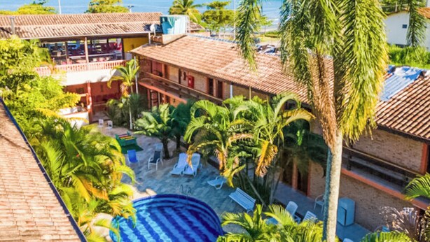 A resort with a swimming pool, palm trees, and a view of the sea. - Hotel Dellamares (Ubatuba)