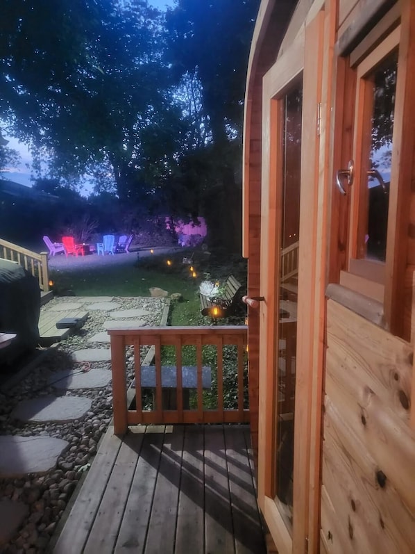 A wooden deck with a railing, a stone pathway, and outdoor seating with neon lights.