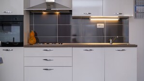 Une cuisine moderne avec des armoires blanches, une hotte de cuisinière en acier inoxydable et un four encastré.