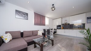 Un salon moderne avec une table basse en verre, un canapé marron et un coin repas comprenant une table et des chaises blanches.