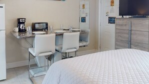 Et hotelværelse med en seng, et spiseområde med bord og stole, en kaffemaskine, en brødrister og et fjernsyn.