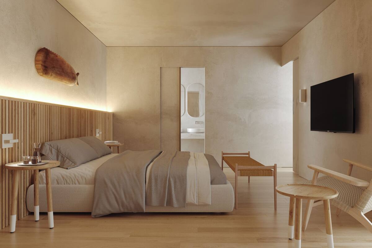 A modern bedroom with a wooden headboard, a bed with a striped blanket, a bedside table with glasses and a pitcher, a wooden chair, a small table, and a TV mounted on the wall.