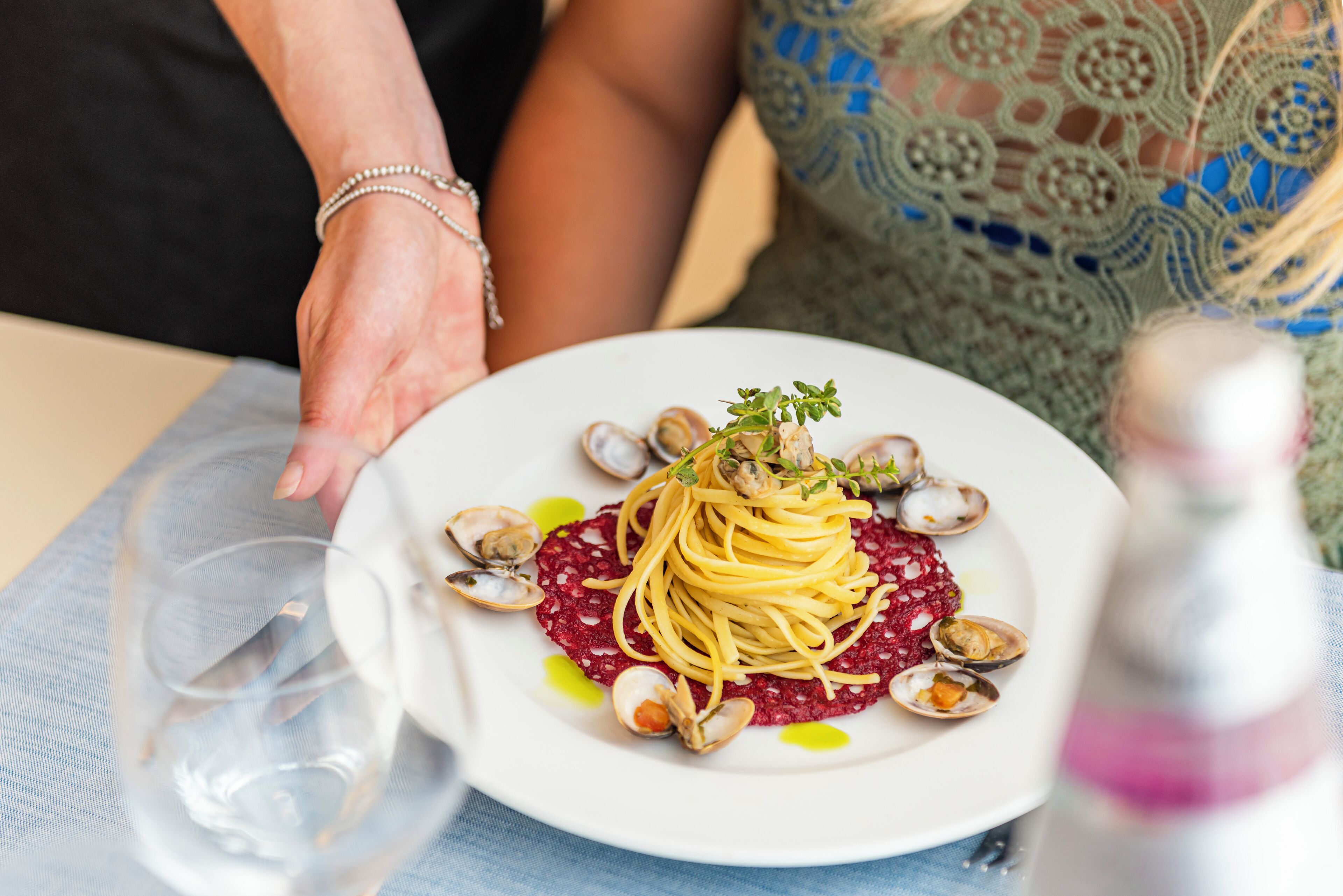Un piatto di pasta con vongole, una guarnizione, un bicchiere di vino e una bottiglia di vino su un tavolo.