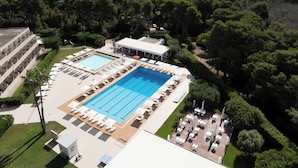 Vue aérienne d’un complexe hôtelier doté d’une grande piscine, de transats et offrant une vue sur la mer.