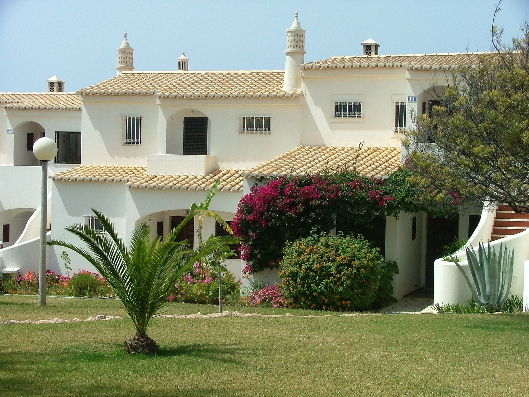 A white building with a tiled roof, multiple chimneys, and a small balcony.